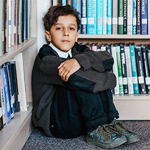 Young boy sat huddled surrounded by shelves of books 